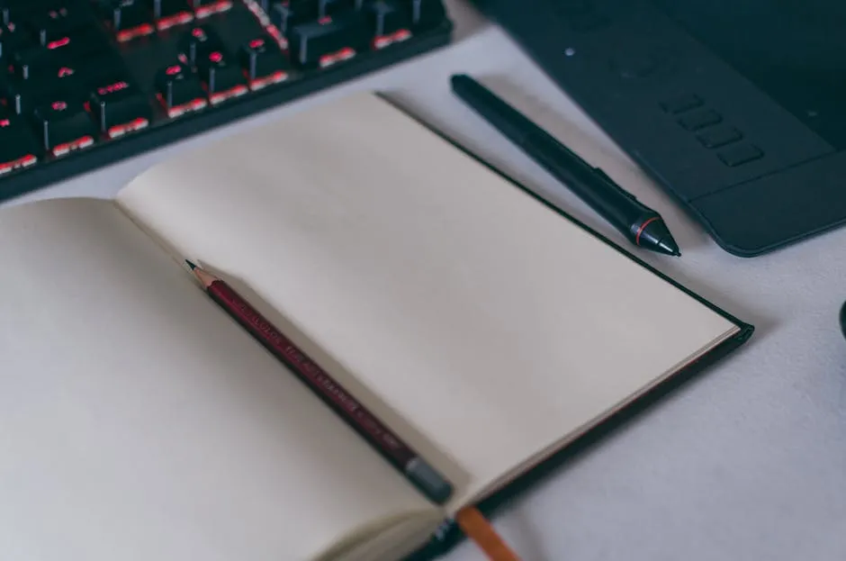 An open paper notebook beside a tablet with a stylus on a wooden desk, suggesting the overlap between handwritten and digital note-taking