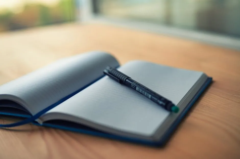 An open paper notebook on a wooden desk, a pen across one page, soft morning light