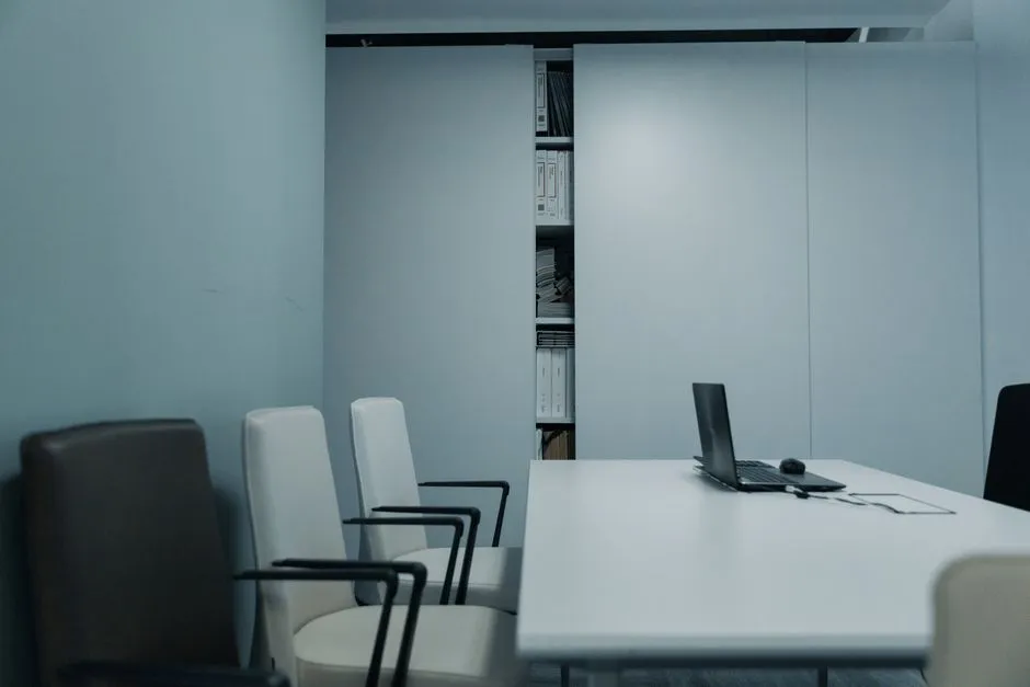 An empty meeting room with a long table and vacant chairs, lit by daylight from a window
