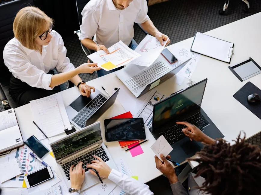 A small cross-functional team gathered around a desk with laptops and documents, suggesting a working specification being reviewed together