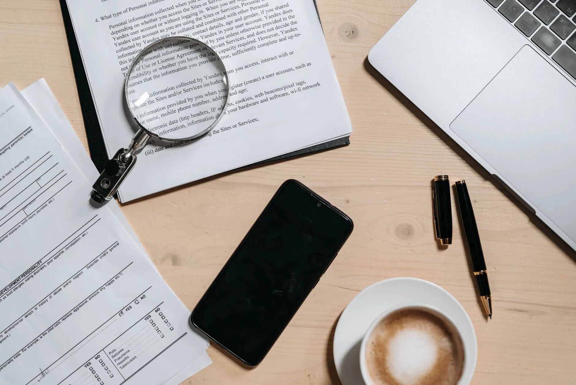 An open laptop on a desk beside a stack of printed documents and folders