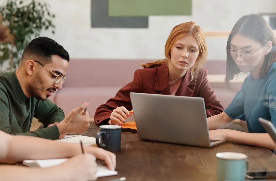 A team gathered around a table with open laptops and notes, several people collaborating at once