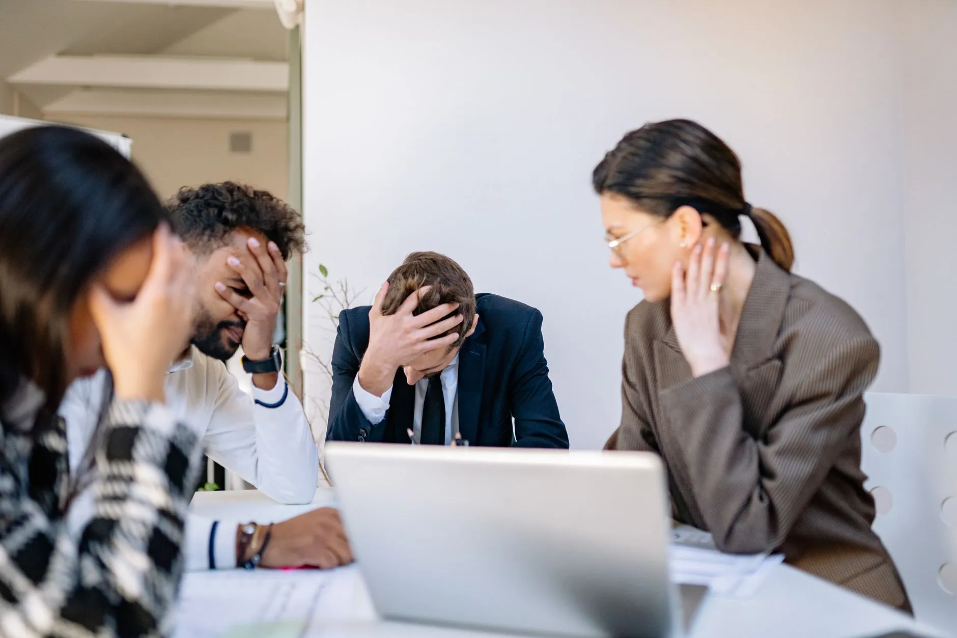 A small team at an office desk looking stressed and overwhelmed while working at a laptop
