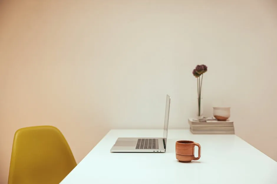 An open laptop, a notebook, and a coffee cup arranged on a clean desk, suggesting a remote-work setup