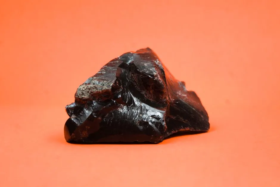 A sharp-edged piece of black obsidian volcanic glass on a neutral surface
